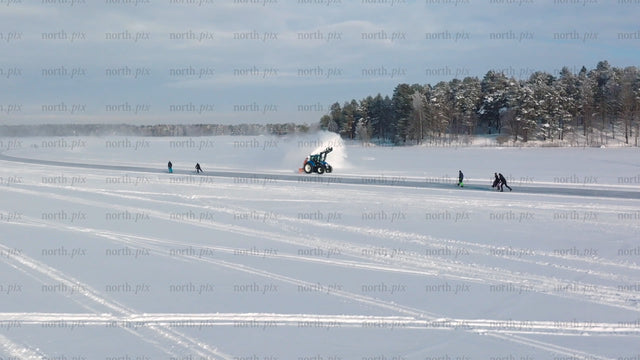 Tractor clearing snow on frozen lake in Luleå, with people skating and kick sledding