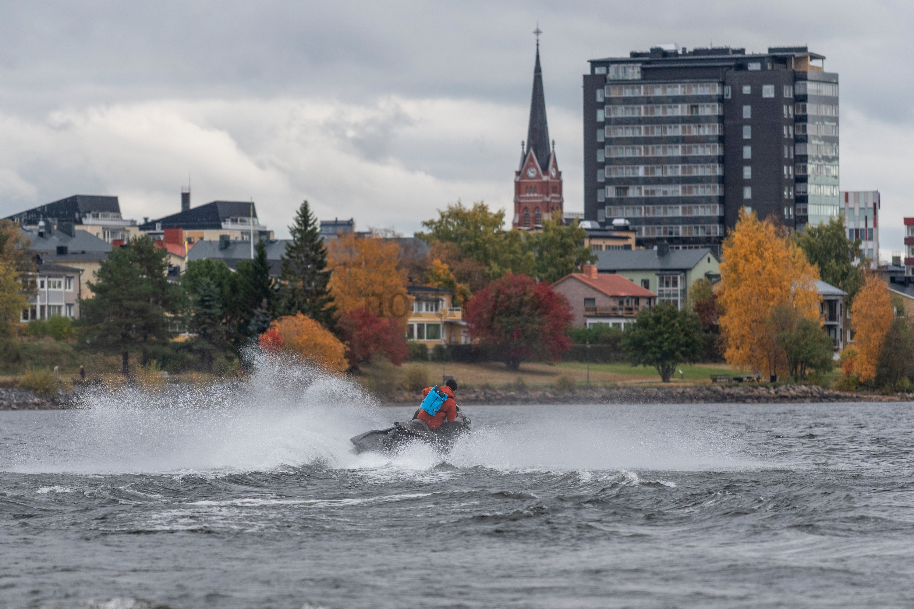 Person on jet ski near waterfront town in autumn