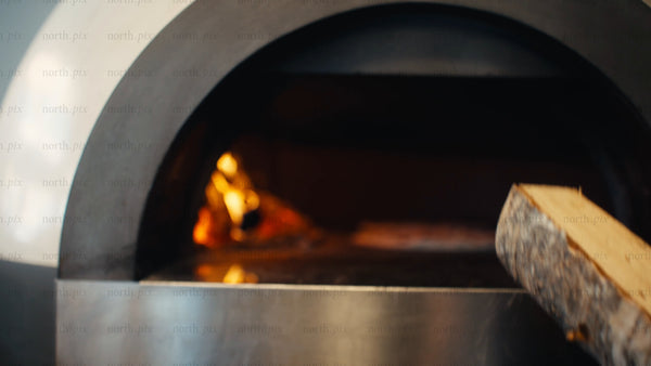 Chef adds wood to fire in brick oven while baking pizza: Slow motion close-up
