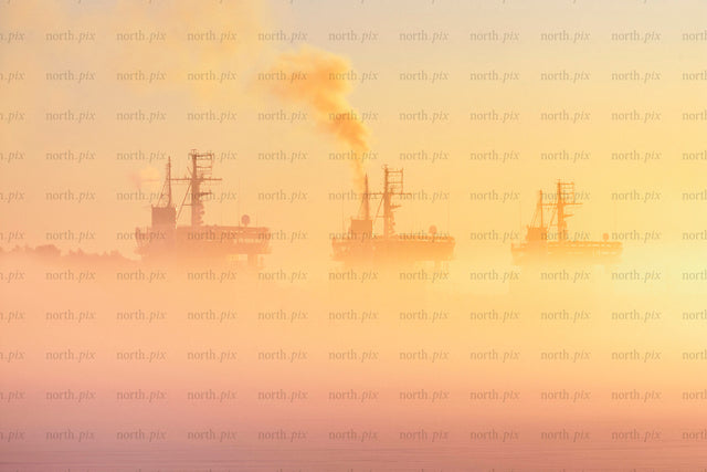 Three icebreakers in fog at sunrise