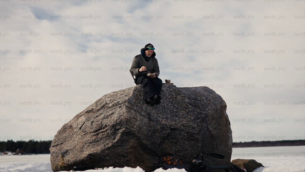 Man eats lunch by fire on frozen Luleå archipelago, in winter