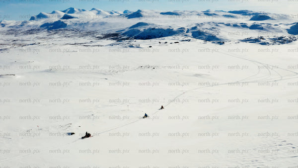 Snowmobiles riding across snowy landscape with mountains