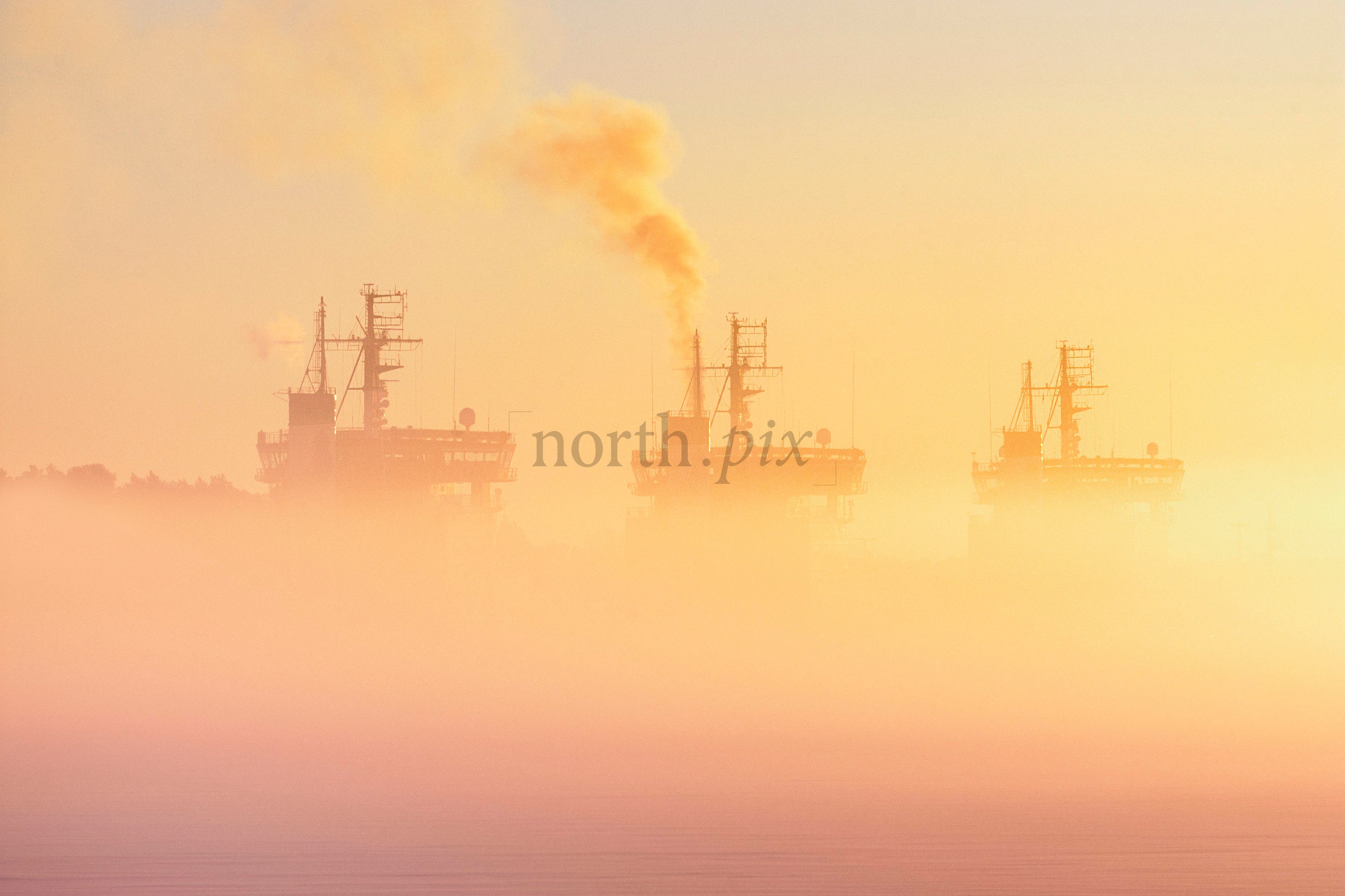Three icebreakers in fog at sunrise