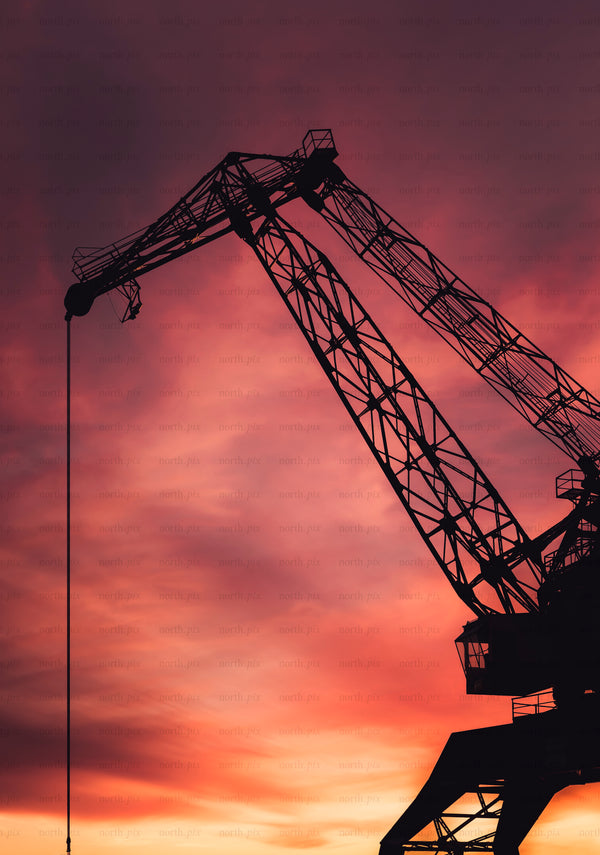 Silhouette of industrial crane against sunset sky