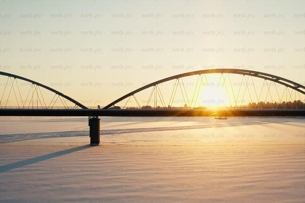 Sunset over snowy river with modern arch bridge in Luleå city center