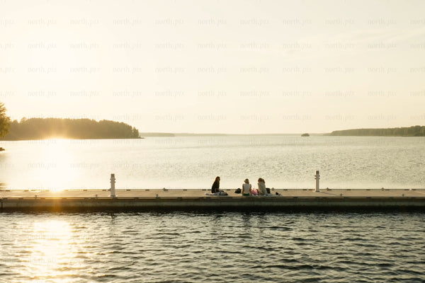 Sunset on the pier at the lake with people sitting and watching the water