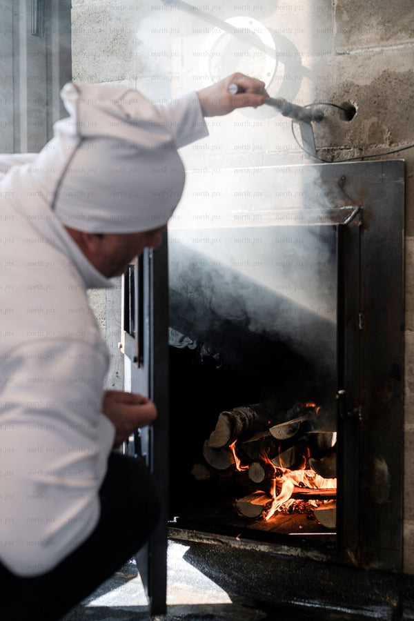 Chef tending wood-fired oven with burning logs