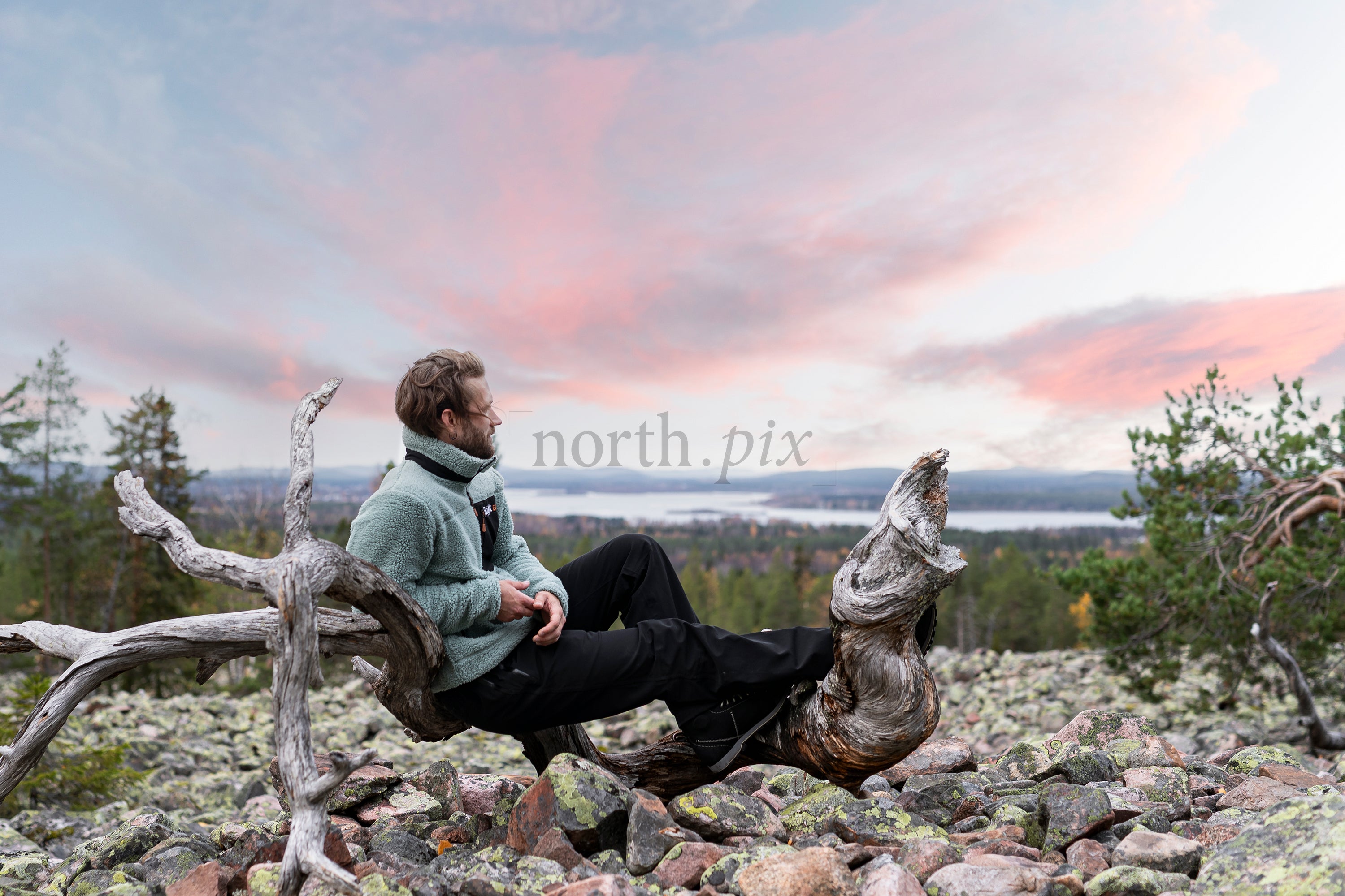 Man sitting on deadwood log on rocky hillside at sunset