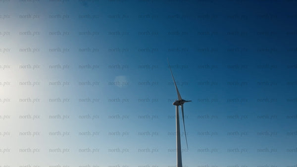 Wind turbine rotating against blue sky with sun, low angle view in winter
