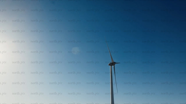 Wind turbine rotating against blue sky with sun, low angle view in winter