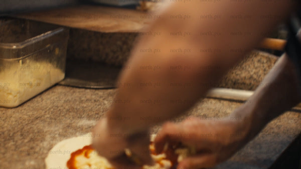 Chef prepares pizza with tomato sauce, mozzarella, and bell peppers in a professional kitchen