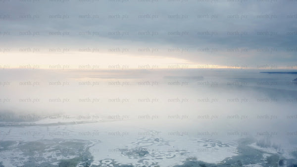 Aerial view of Piteå Haraholmen in winter: Snowy landscape, icy sea, and coastal fog