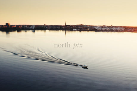 Boat Glides Across Calm Water Toward Luleå City Center at Sunset