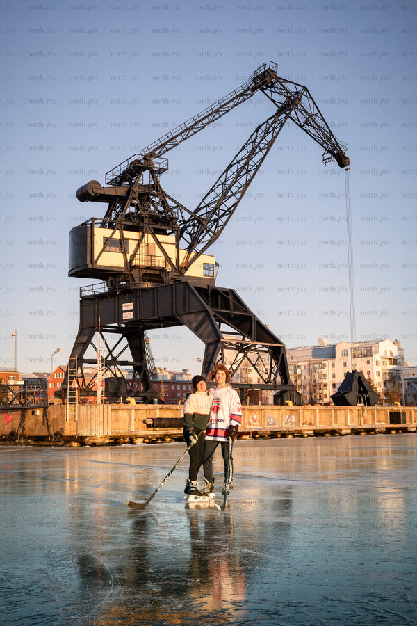 Two people playing ice hockey by harbor crane at sunset