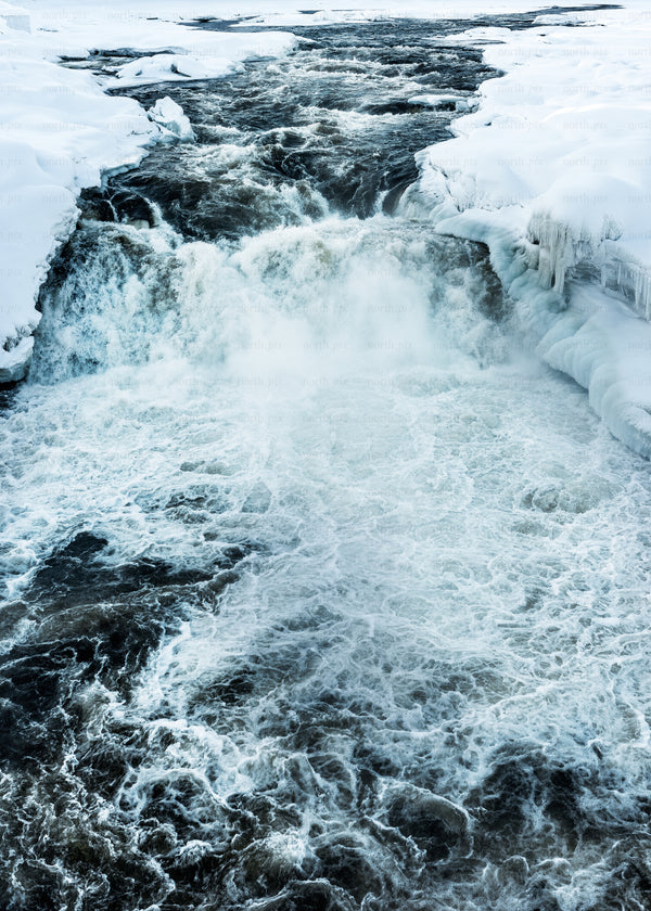 Icy waterfall and river flowing through snow-covered banks