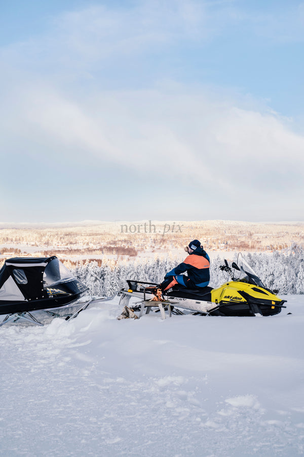 Snowmobile rider overlooking snowy valley at sunrise