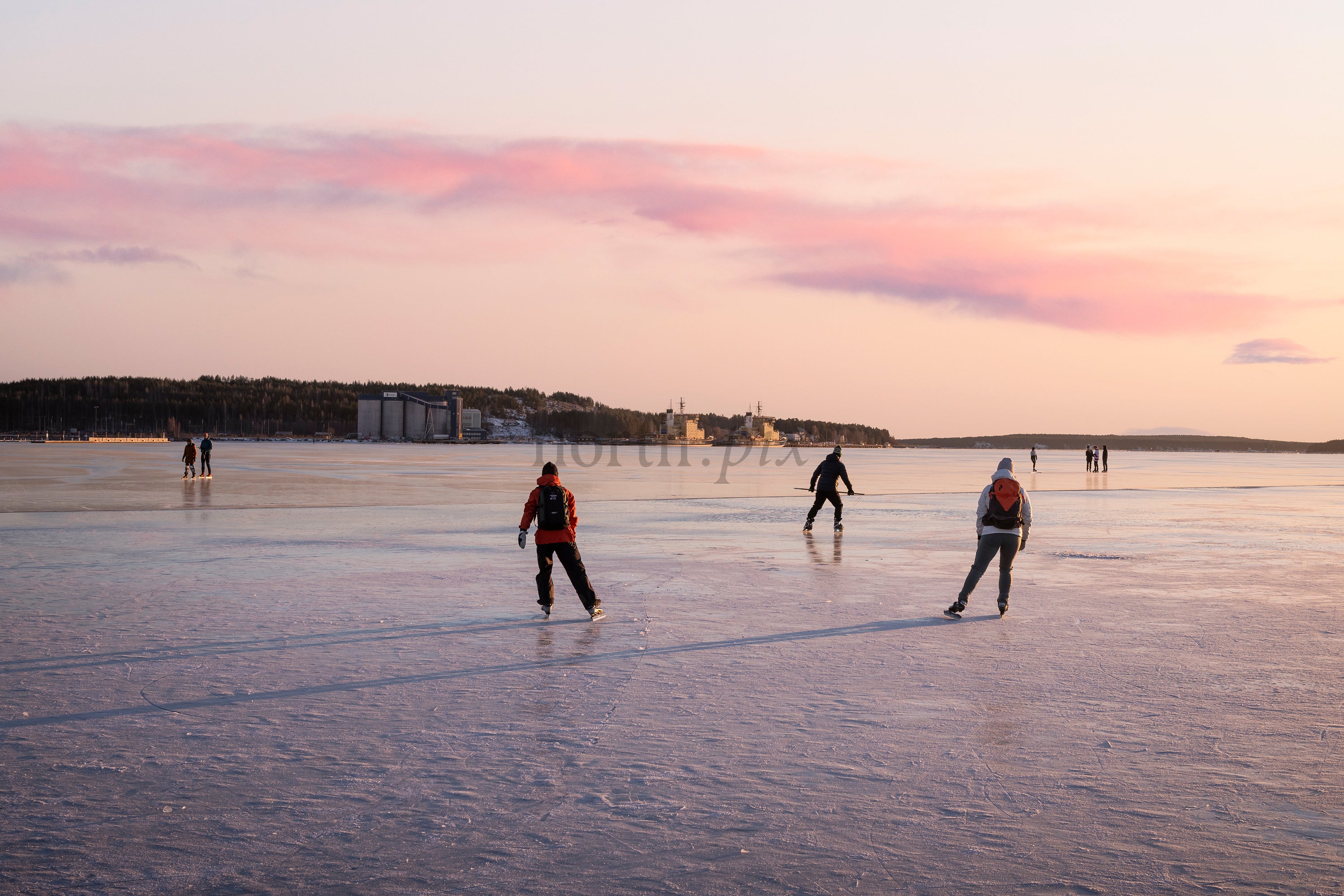 People ice skating on frozen sea at sunset