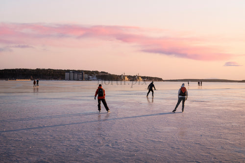 People ice skating on frozen sea at sunset