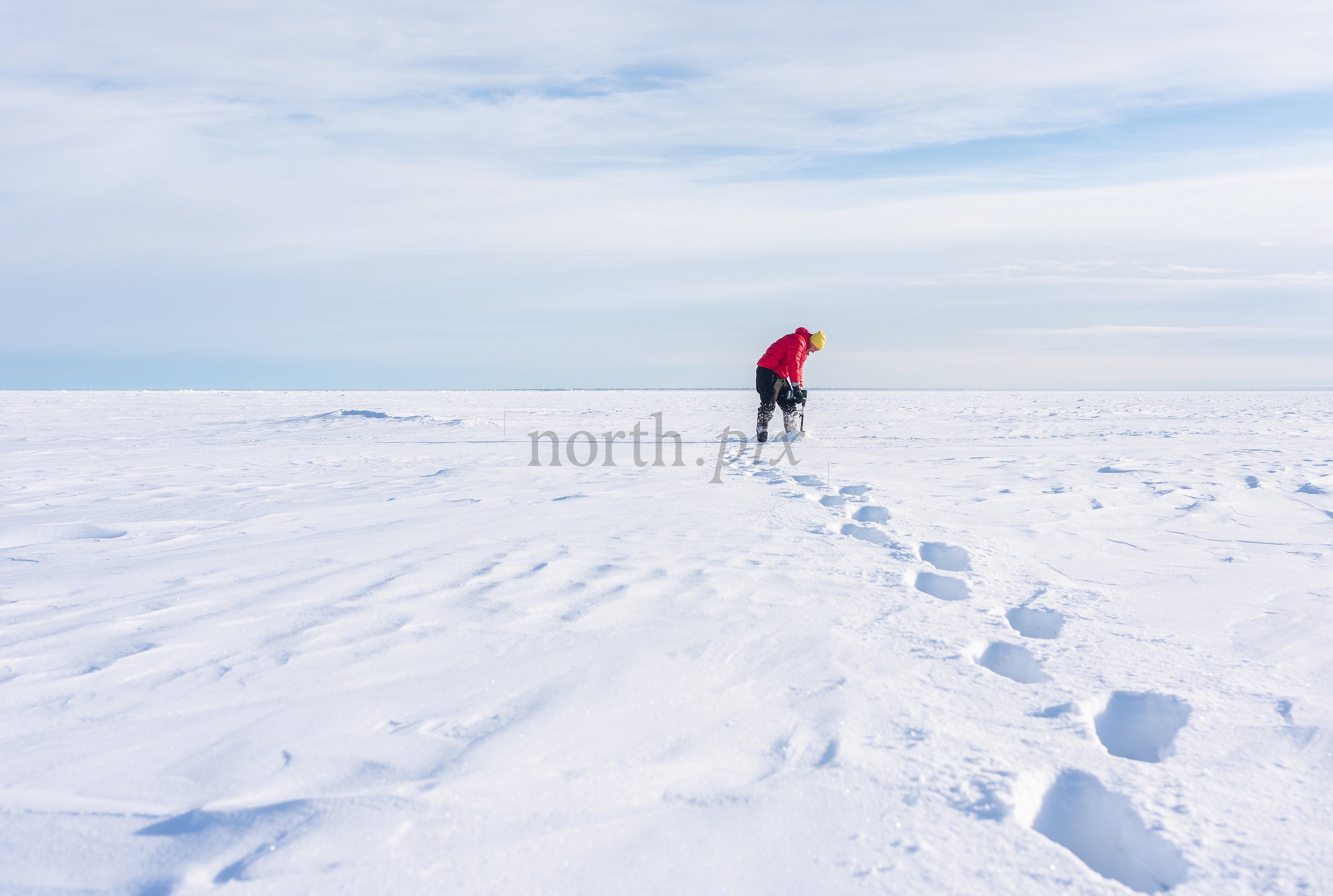 Person drilling ice on frozen lake at midday