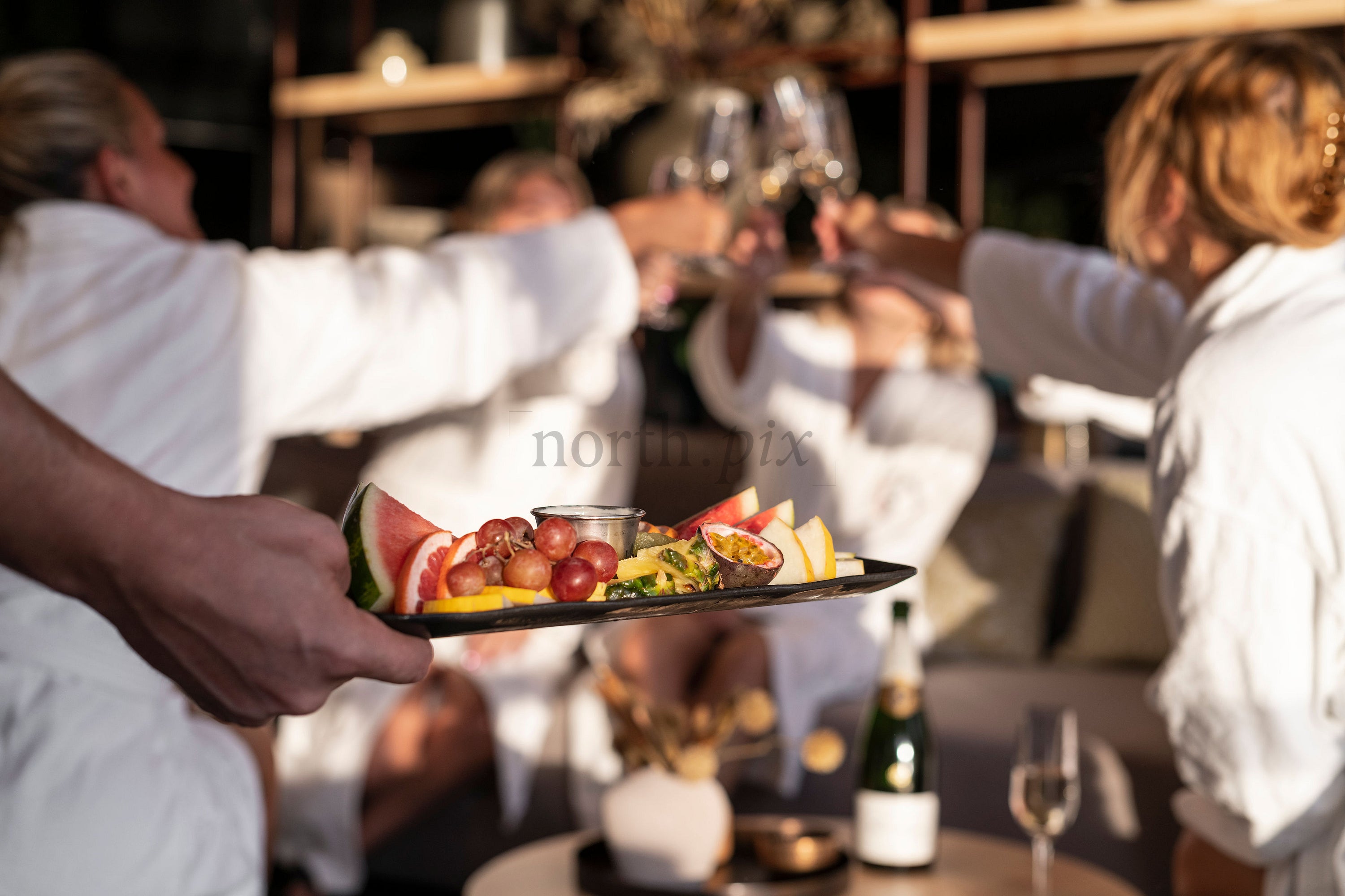 Women in robes toasting with wine and fruit platter