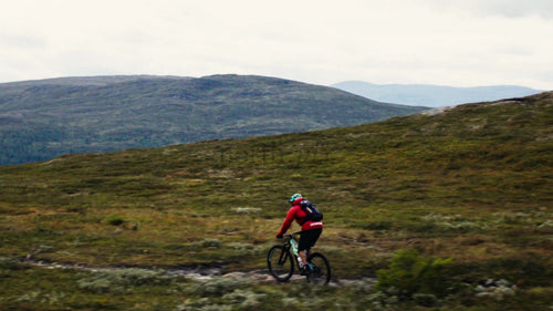 Man cyklar mountainbike nerför stenig terräng i naturskön dal