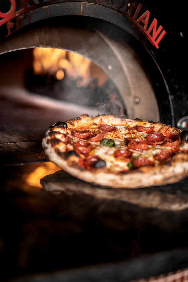 Wood-fired pepperoni pizza baking in oven