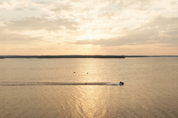 Golden sunset over calm lake with boat wake and distant island shoreline at Luleå city center