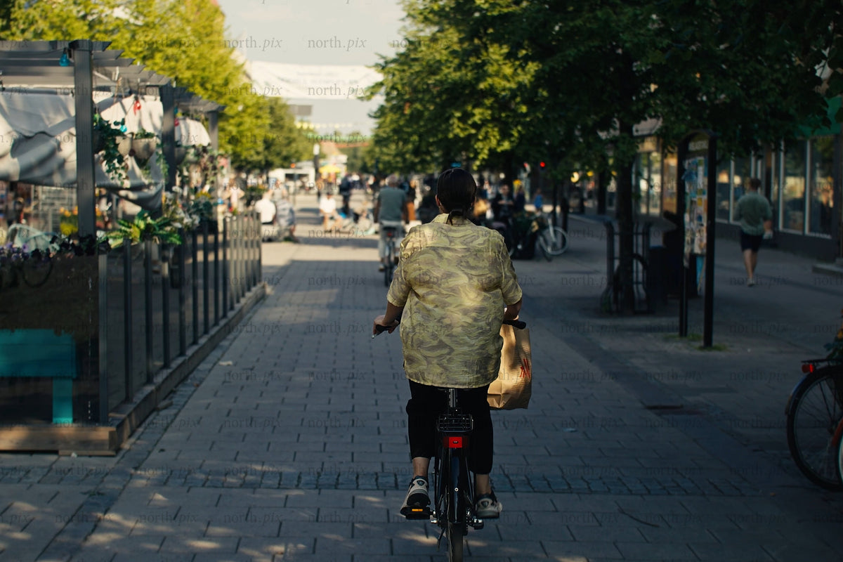 Cyklist som cyklar genom Luleå centrum med uteserveringar och livlig gågata