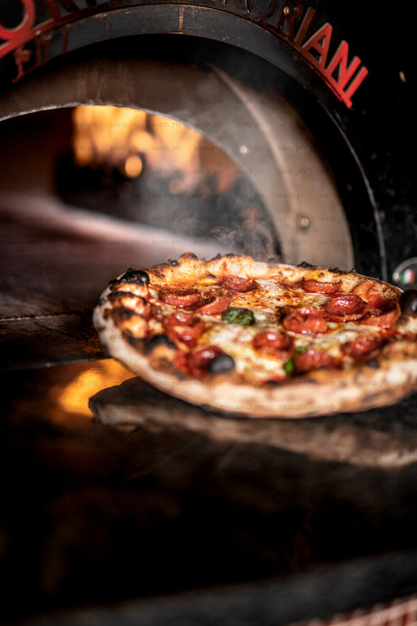 Wood-fired pepperoni pizza baking in oven