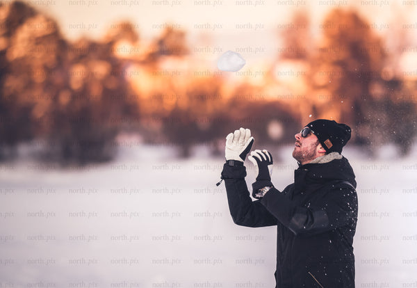 Man catching a snowball in a snowy field at sunset