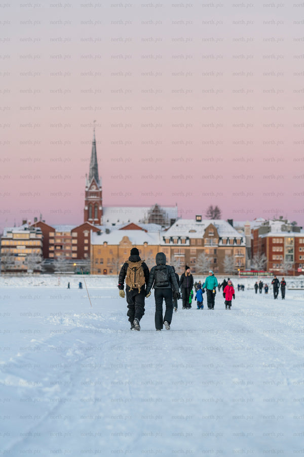 Two people walking on ice road toward snowy city