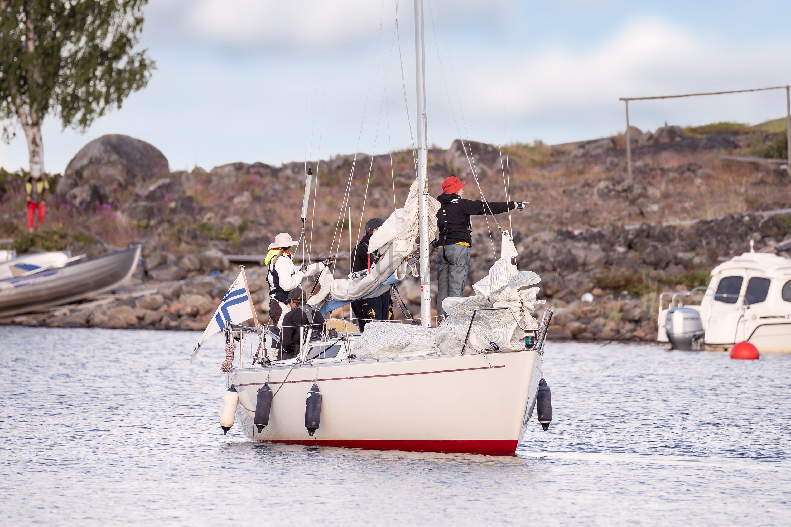 Sailboat with crew near rocky shore in daylight