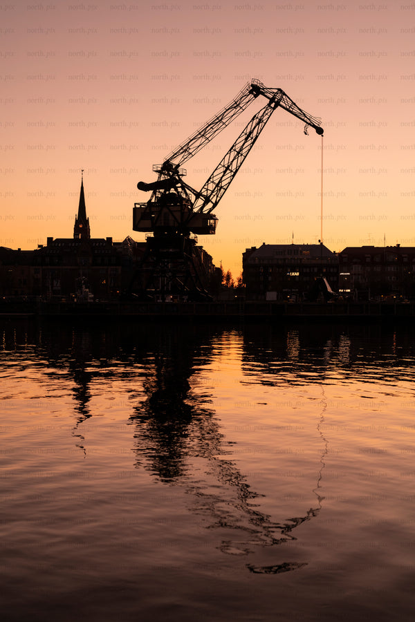Silhouette of harbor crane and city at sunset