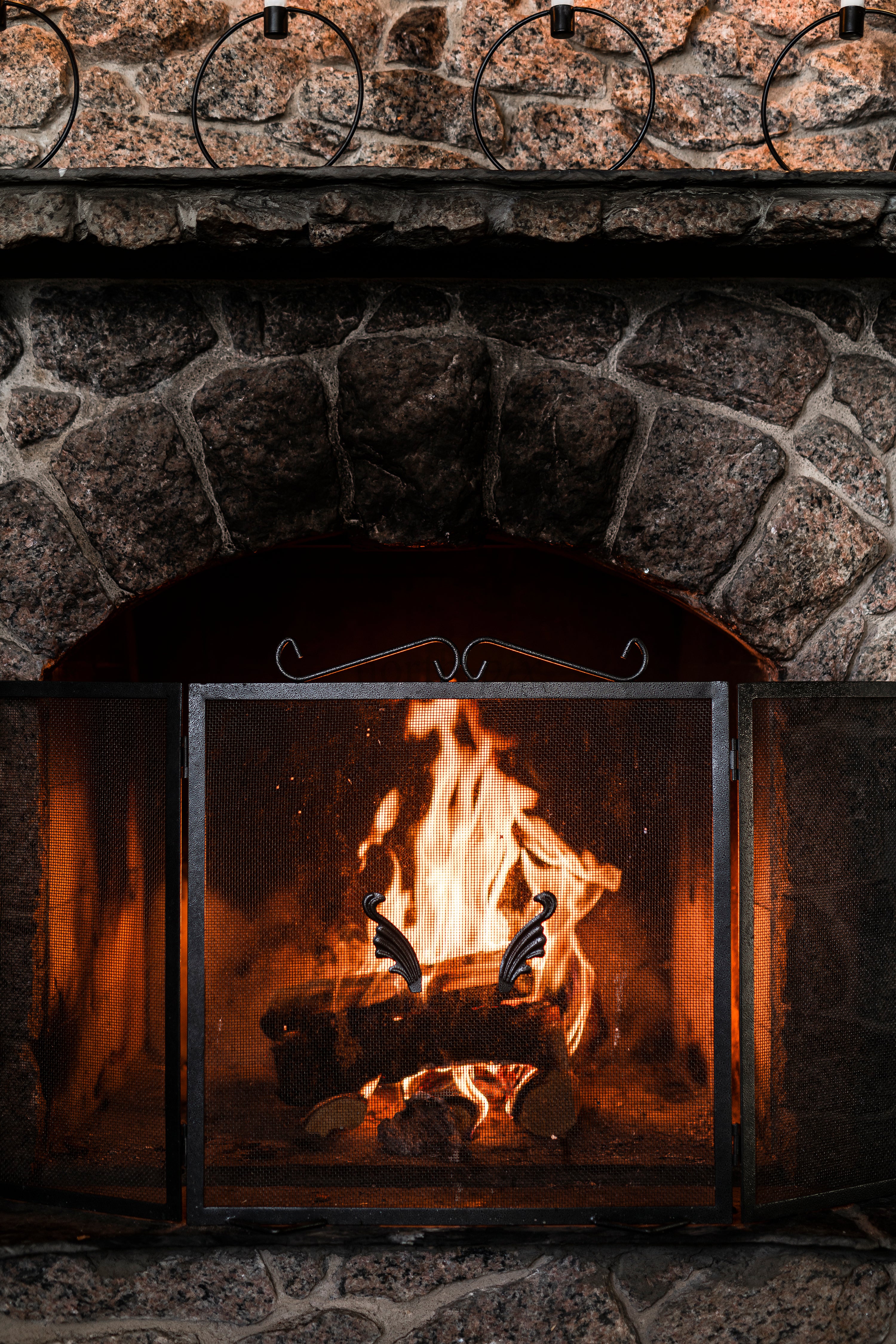 Stone fireplace with burning logs and metal screen