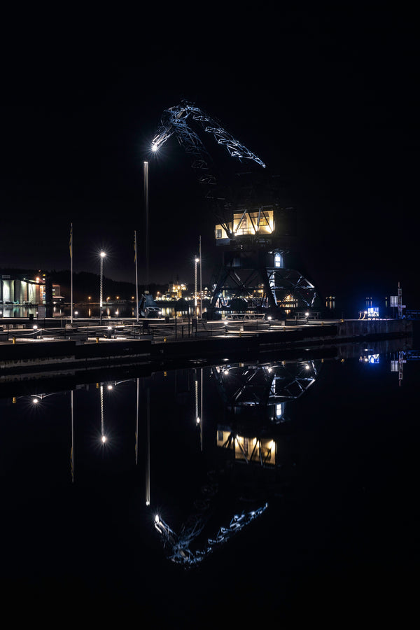 Illuminated harbor crane reflected in calm night water