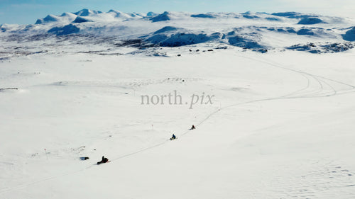 Snöskotrar som kör över snöigt landskap med majestätiska berg