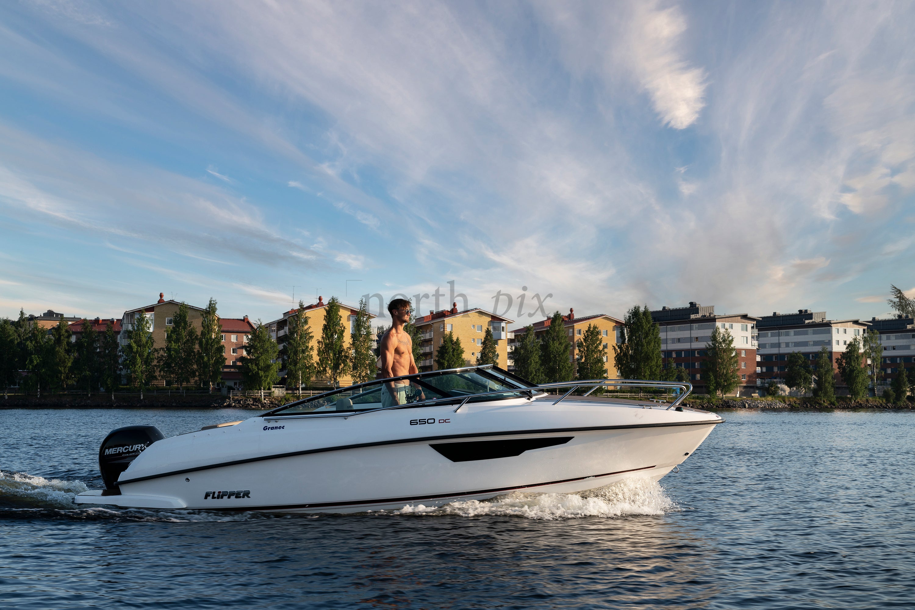 Man steering motorboat by riverside apartment buildings at sunset