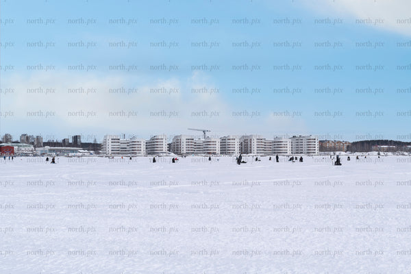 People ice fishing on frozen bay with waterfront apartments, winter