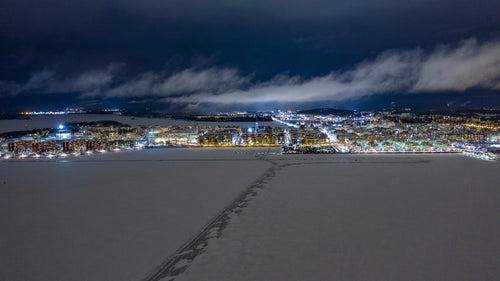 Luleå, Sverige på natten: Flygdrönare med timelapse av stadskärnan med fyrverkerier över frusen sjö på vintern