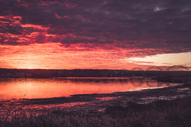 Arched bridge over river under red sunset sky