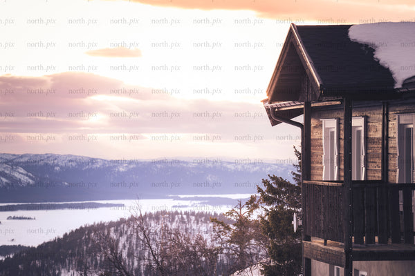 Wooden cabin balcony overlooking snowy lake at sunset
