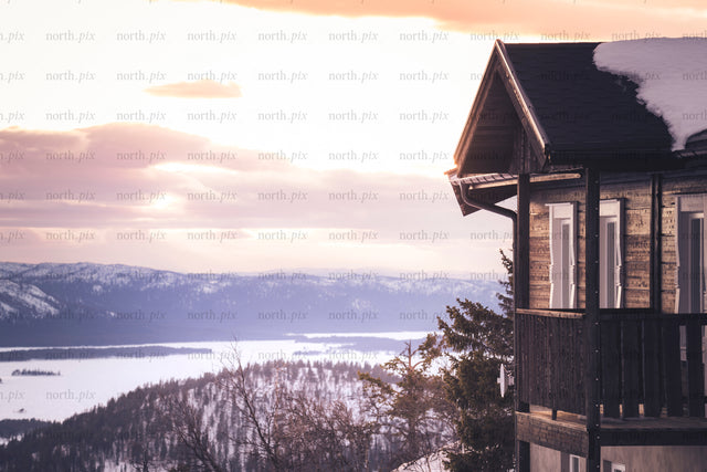 Wooden cabin balcony overlooking snowy lake at sunset