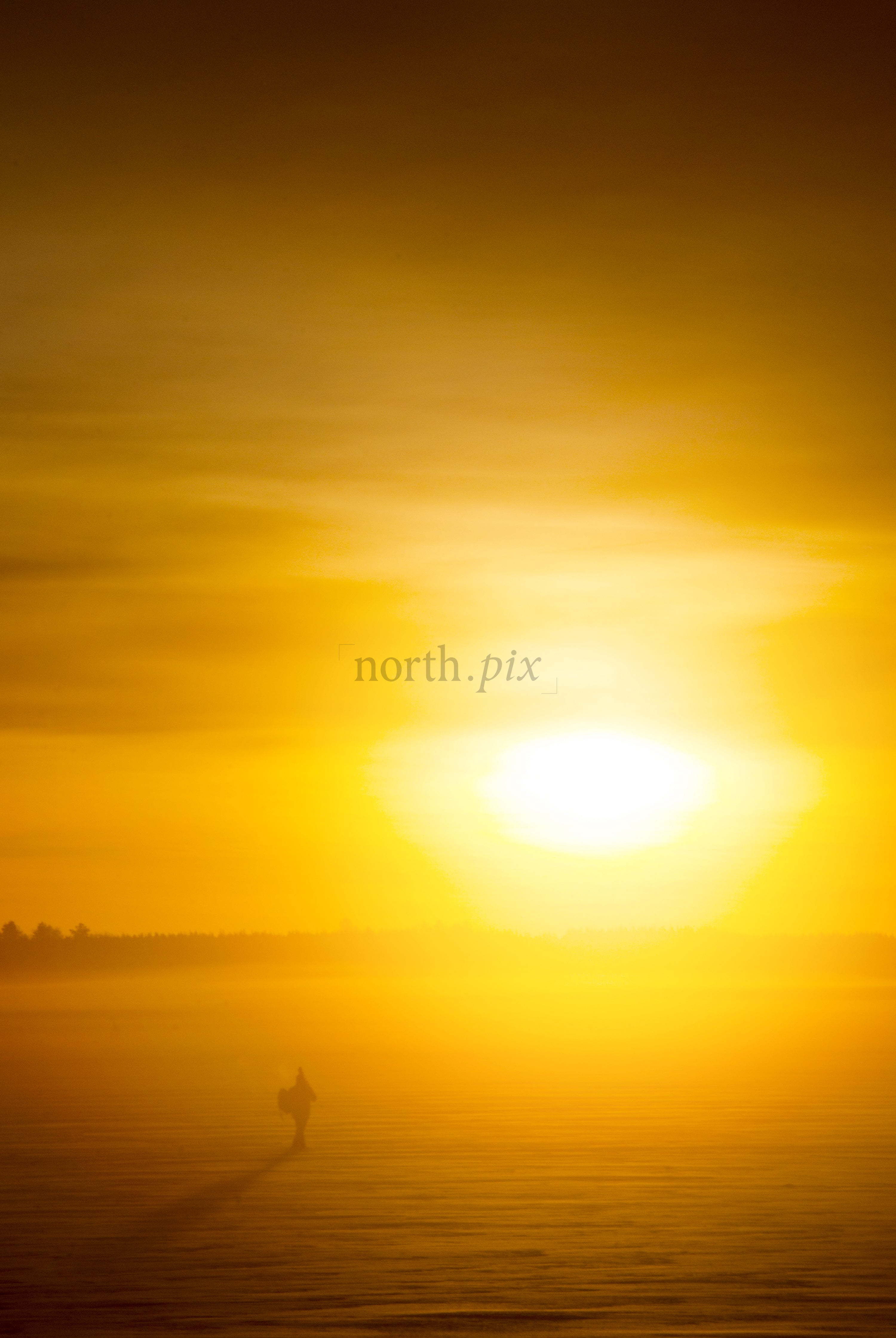 Fisherman walking on frozen lake at sunrise