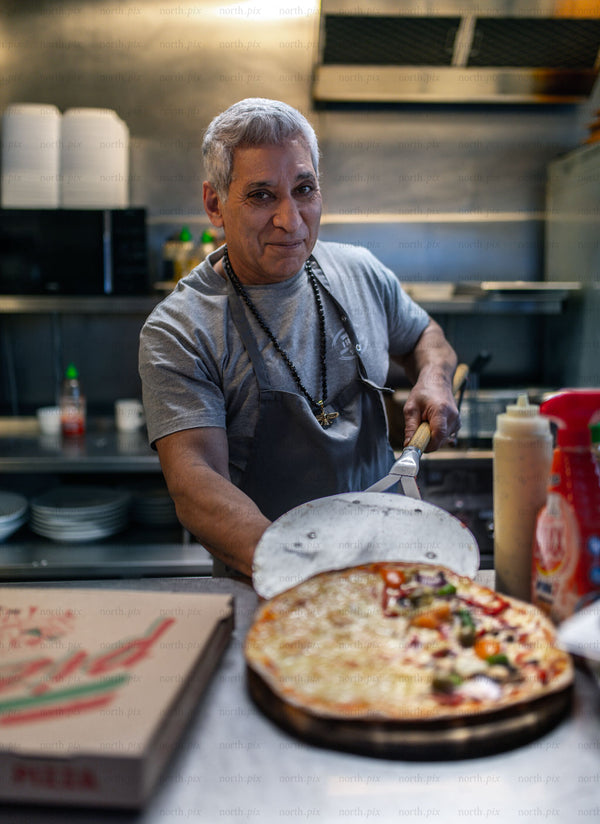 Pizza chef serving pizza in a commercial kitchen, evening