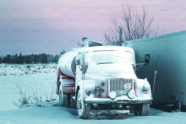 Snow-covered vintage tanker truck parked at dusk