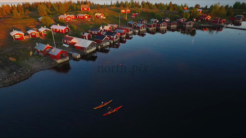 Kajakpaddlare paddlar förbi röda stugor i Luleå skärgård i solnedgången