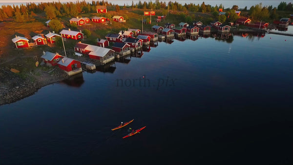 Kayakers Paddle Past Red Cabins in the Luleå Archipelago at Sunset
