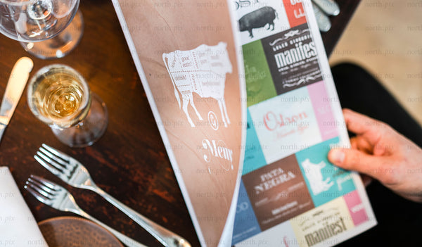 Person reading a restaurant menu at table, close-up