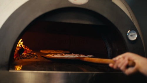 Kocken lägger pizzor i vedeldad ugn i restaurangkök