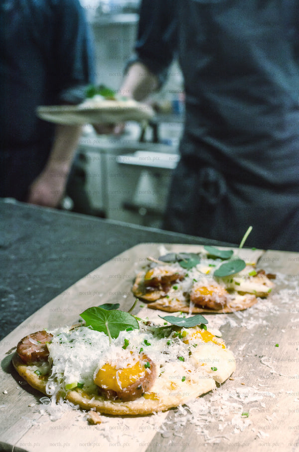 Chefs plating flatbread with cheese in a kitchen